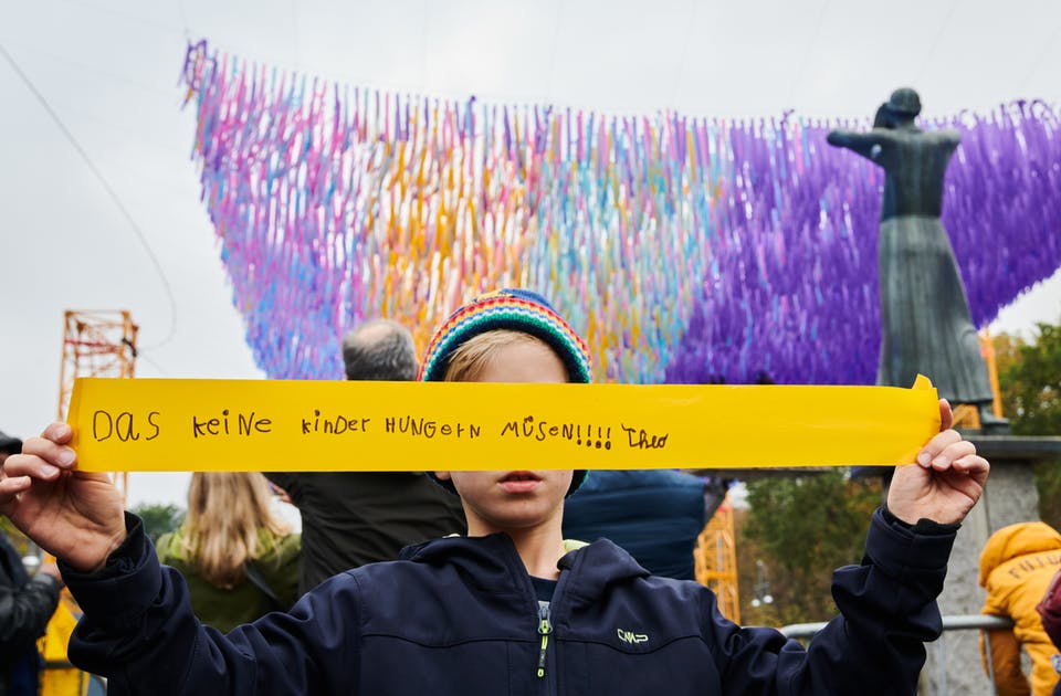 Visions in Motion in front of Brandenburg Gate in Berlin Germany. Boy holding up the message he wrote on his streamer.